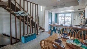Un intérieur de maison comprenant un escalier, un coin repas, une cuisine et une vue sur l’extérieur.