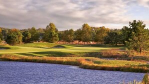Un parcours de golf avec un plan d’eau au premier plan, entouré d’arbres et de zones herbeuses.