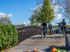 Un puente de madera con barandillas de metal, rodeado de vegetación y edificios residenciales.