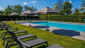 A swimming pool with lounge chairs and umbrellas, surrounded by a hedge and trees. - Nice Chalet on a Holiday Park 25 km From Amsterdam (Velsen-Zuid)