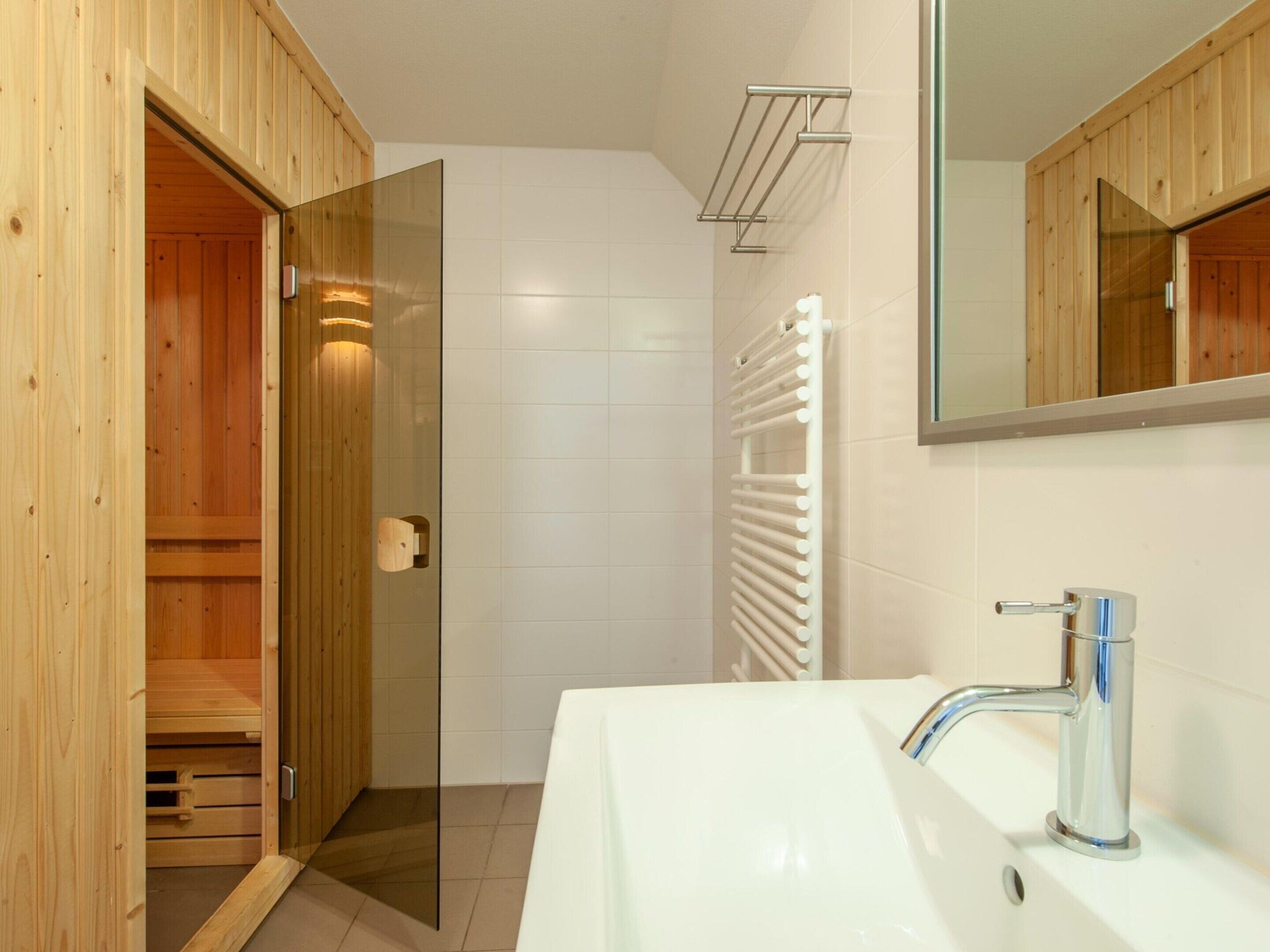 A modern bathroom with a wooden shower enclosure, a white sink with a chrome faucet, and a white towel rack.