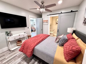 A bedroom with a bed, a TV, a ceiling fan, a wardrobe, and a bathroom visible through an open door. - Historic Atascadero Colony Charmer! (Atascadero)