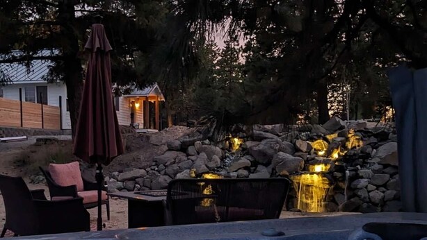 Un jacuzzi con caída de agua, rodeado de mobiliario exterior y un muro de piedra.