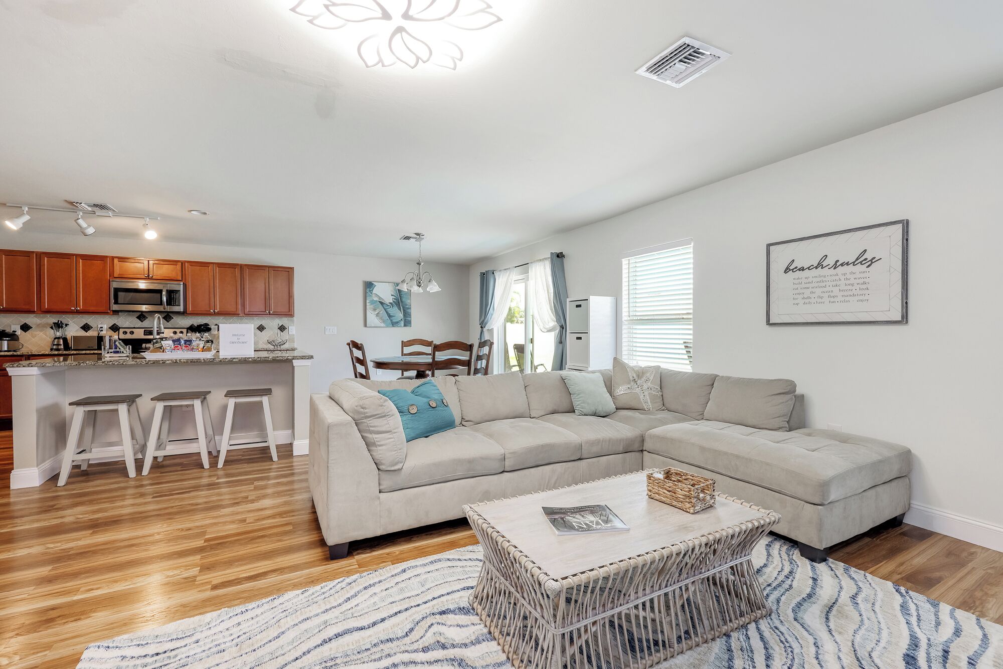 A modern living room with a sectional sofa, a coffee table, and a kitchen area with wooden cabinets and a microwave.