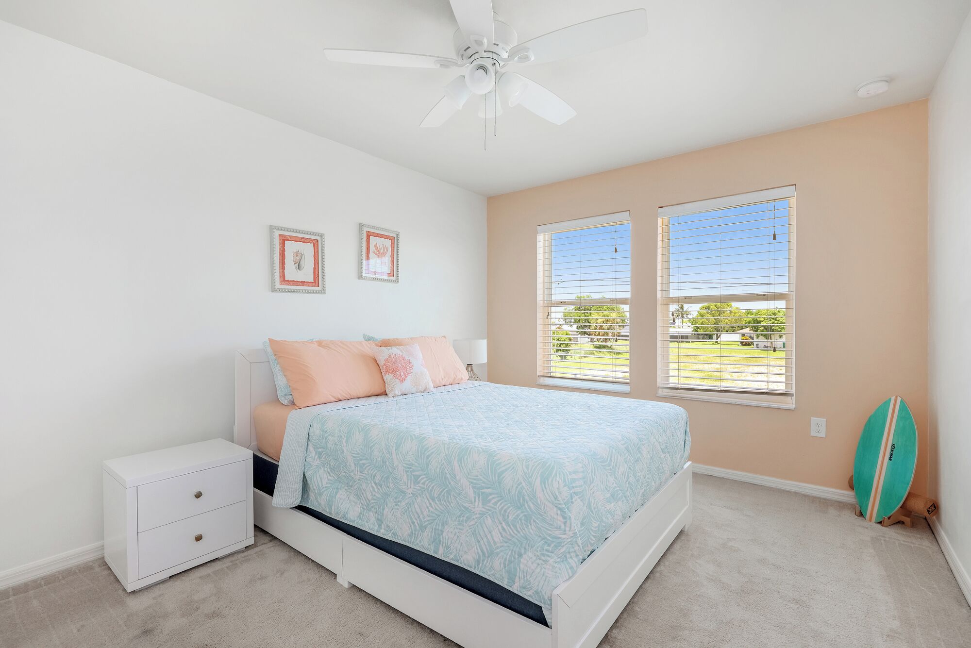 A bedroom with a bed, a nightstand, a ceiling fan, and two windows with blinds.