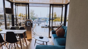 A modern room with a large window overlooking a marina, a dining area with a table and chairs, and a cozy seating area with a sofa and cushions.