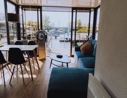 A modern room with a large window overlooking a marina, a dining area with a table and chairs, and a cozy seating area with a sofa and cushions.