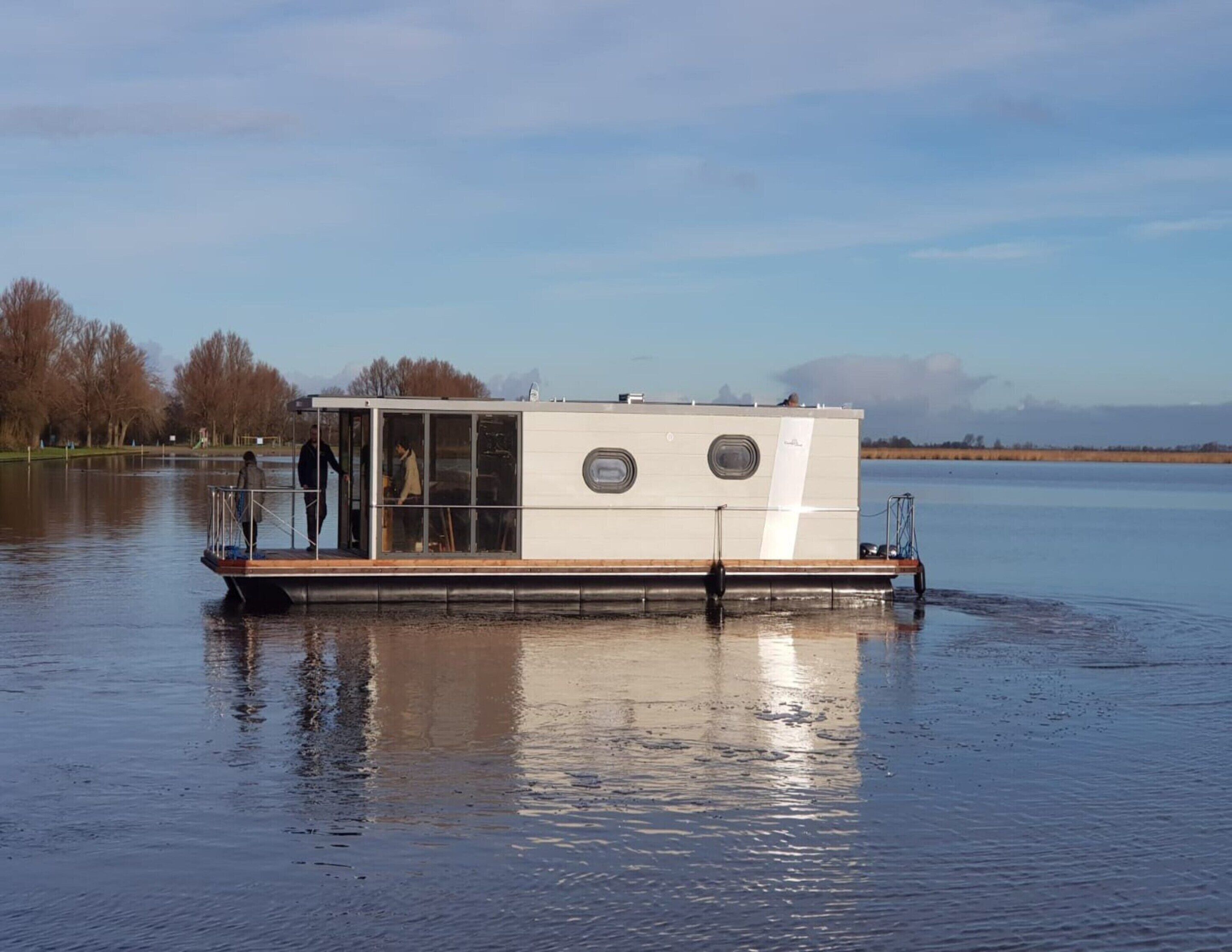 A stationary houseboat with a covered deck and a cabin, floating on calm water.