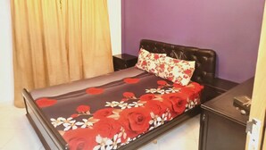Een bed met een bloemenbedekking, een zwart hoofdbord en een nachtkastje met een lamp.
