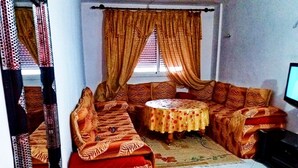 Een woonkamer met een zithoek, een rond salontafeltje en een televisie.