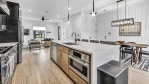 A modern kitchen with a central island, stainless steel appliances, and a dining area with a wooden table and chairs. - Modern Eastside Home with Gourmet Kitchen, 3 Floors, Game Room, Walk to restaurants and bars (Austin)