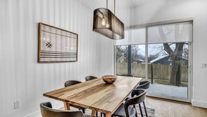 A dining area with a wooden table, black chairs, a hanging light fixture, and a large window with a view of the outdoors. - Modern Eastside Home with Gourmet Kitchen, 3 Floors, Game Room, Walk to restaurants and bars (Austin)