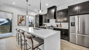 A modern kitchen with a large island, dark cabinetry, stainless steel appliances, and a bar seating area. - Modern Eastside Home with Gourmet Kitchen, 3 Floors, Game Room, Walk to restaurants and bars (Austin)