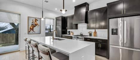 A modern kitchen with a large island, dark cabinetry, stainless steel appliances, and a bar seating area.