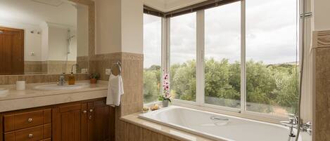 A modern bathroom with a large bathtub, a vanity with a mirror, and a window offering a view of greenery.