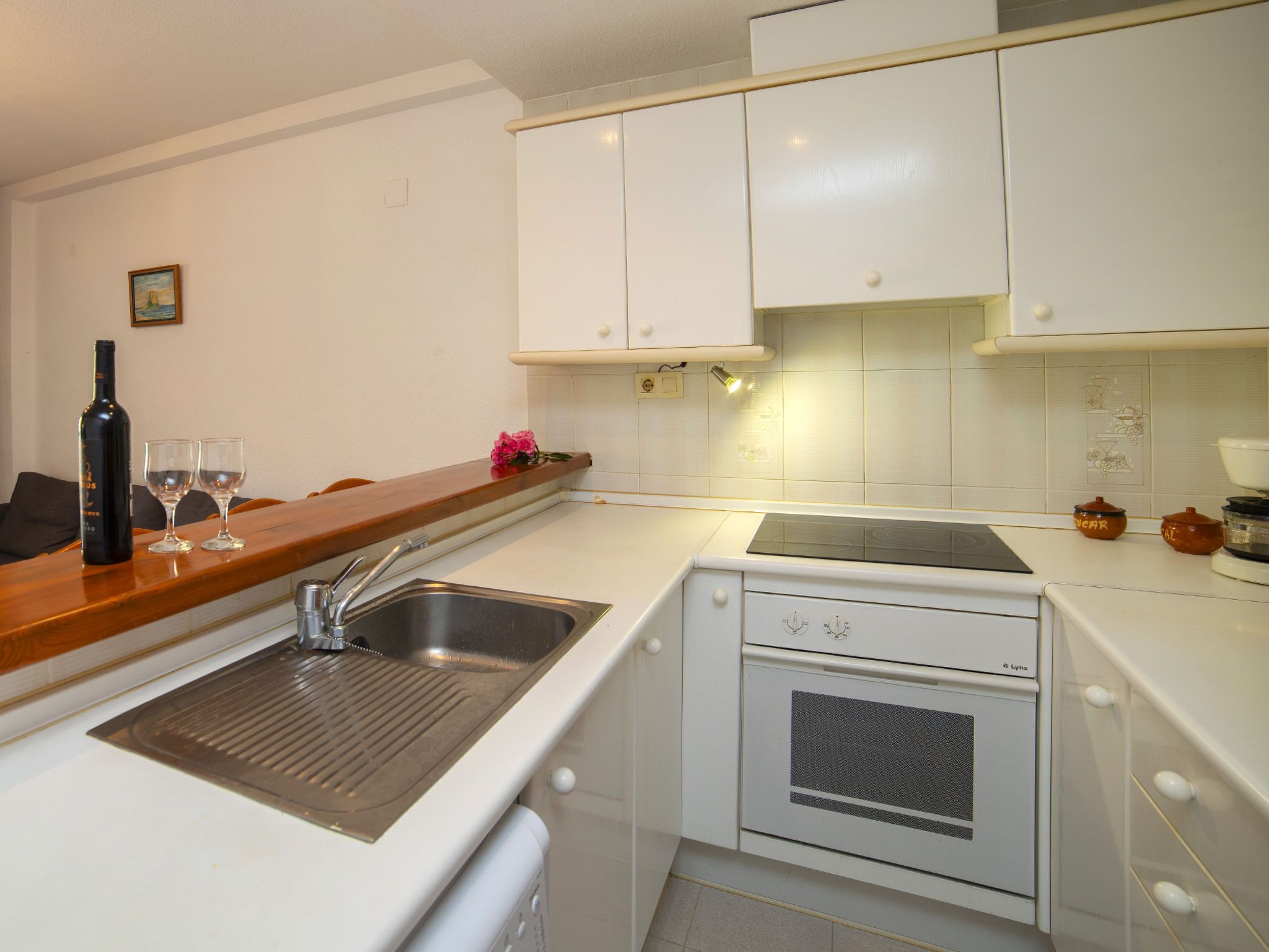 A compact kitchen with white cabinets, a built-in oven, a sink, and a countertop.