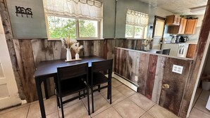 Una cocina con paneles de madera, una mesa de comedor con sillas y una ventana con cortina.
