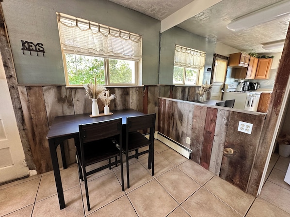 A kitchen with wooden paneling, a dining table with chairs, and a window with a curtain.