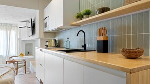 Een moderne keuken met witte kasten, een houten aanrecht, een zwarte kraan en een klein eiland met een spoelbak. Er staan potten met planten op het aanrecht en een mandje op het eiland.