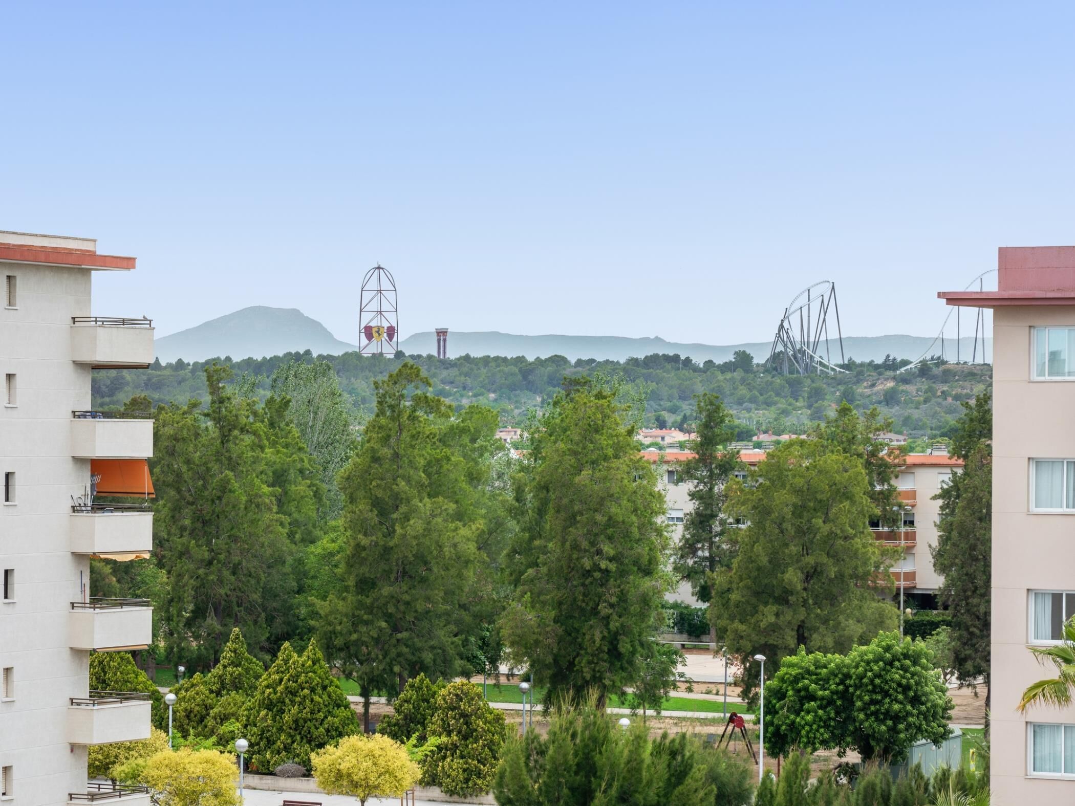 Un quartier résidentiel avec des immeubles modernes, un parc arboré et une vue lointaine sur une montagne.