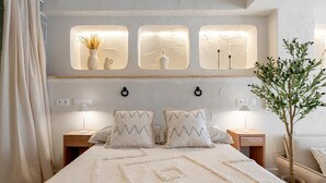 Een slaapkamer met een groot bed, twee nachtkastjes, een wandlamp en een potplant.