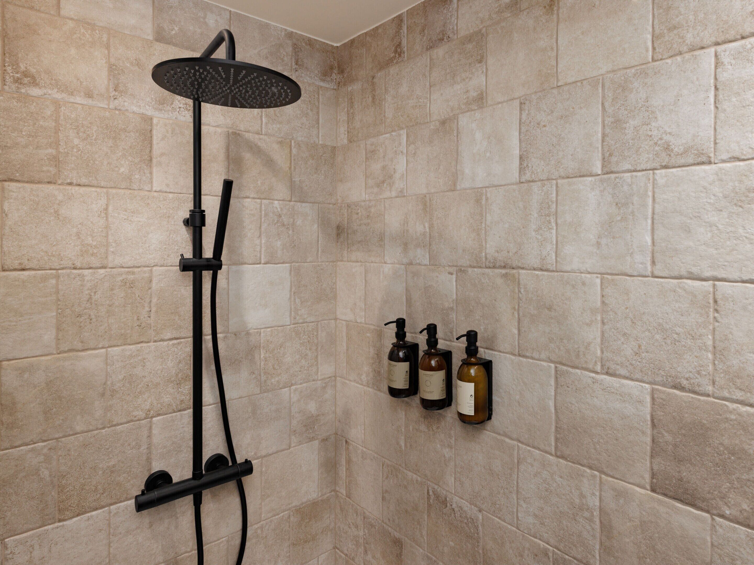 Ducha con cabezal de ducha de lluvia y cabezal de ducha manual, montada en una pared con azulejos.
