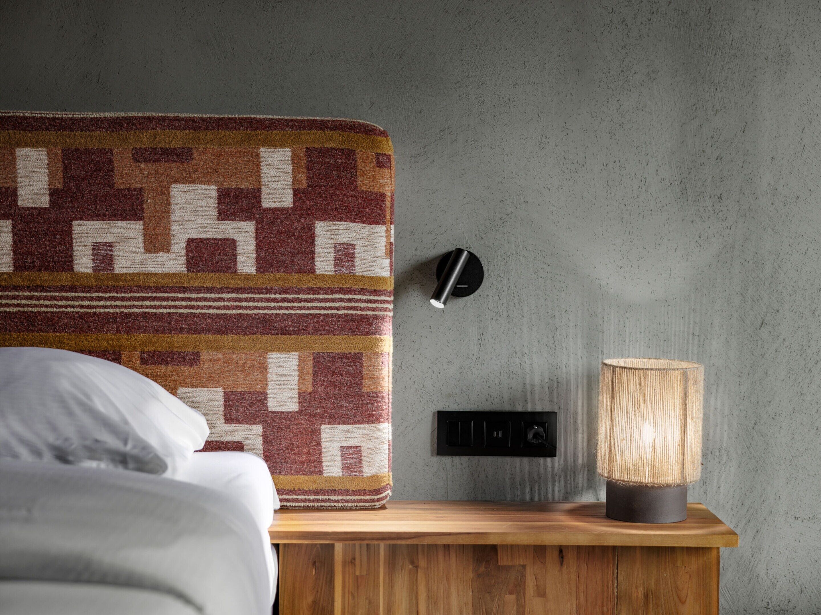 Una camera da letto con una coperta fantasia, una lampada da comodino e un interruttore a parete.
