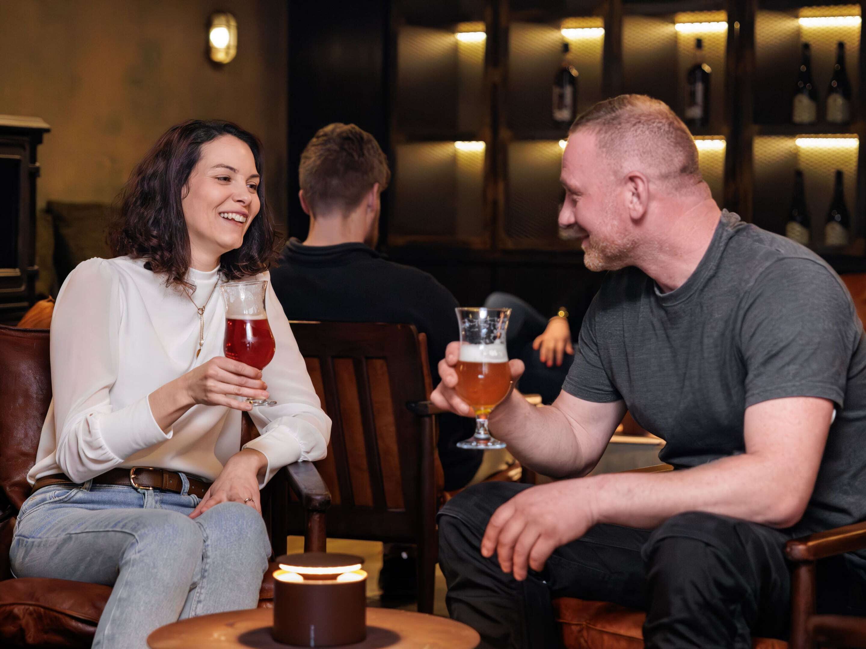 Two people seated in a bar area with a small table and a candle in the foreground.