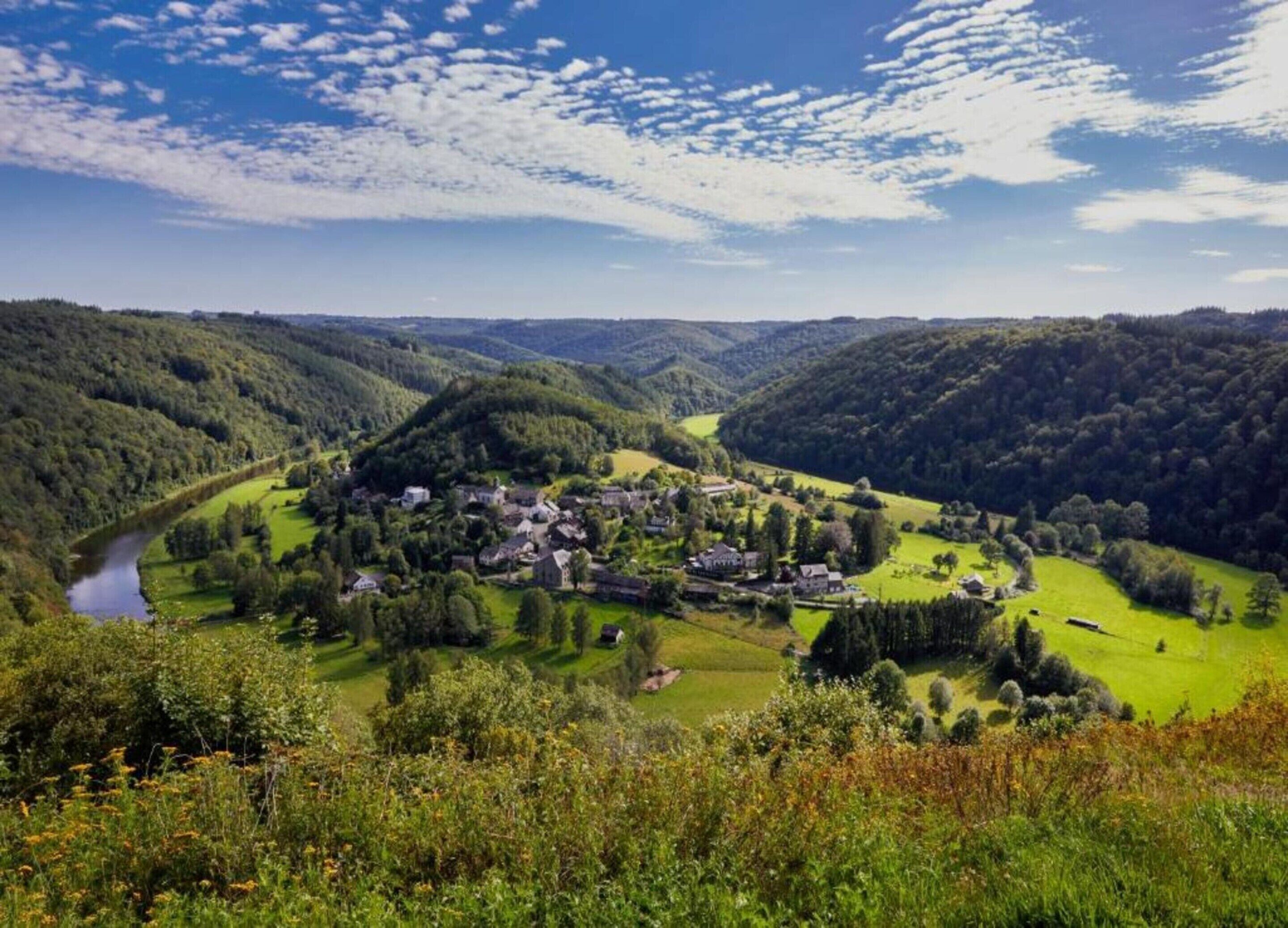 A village nestled in a valley with a river, surrounded by forested hills.
