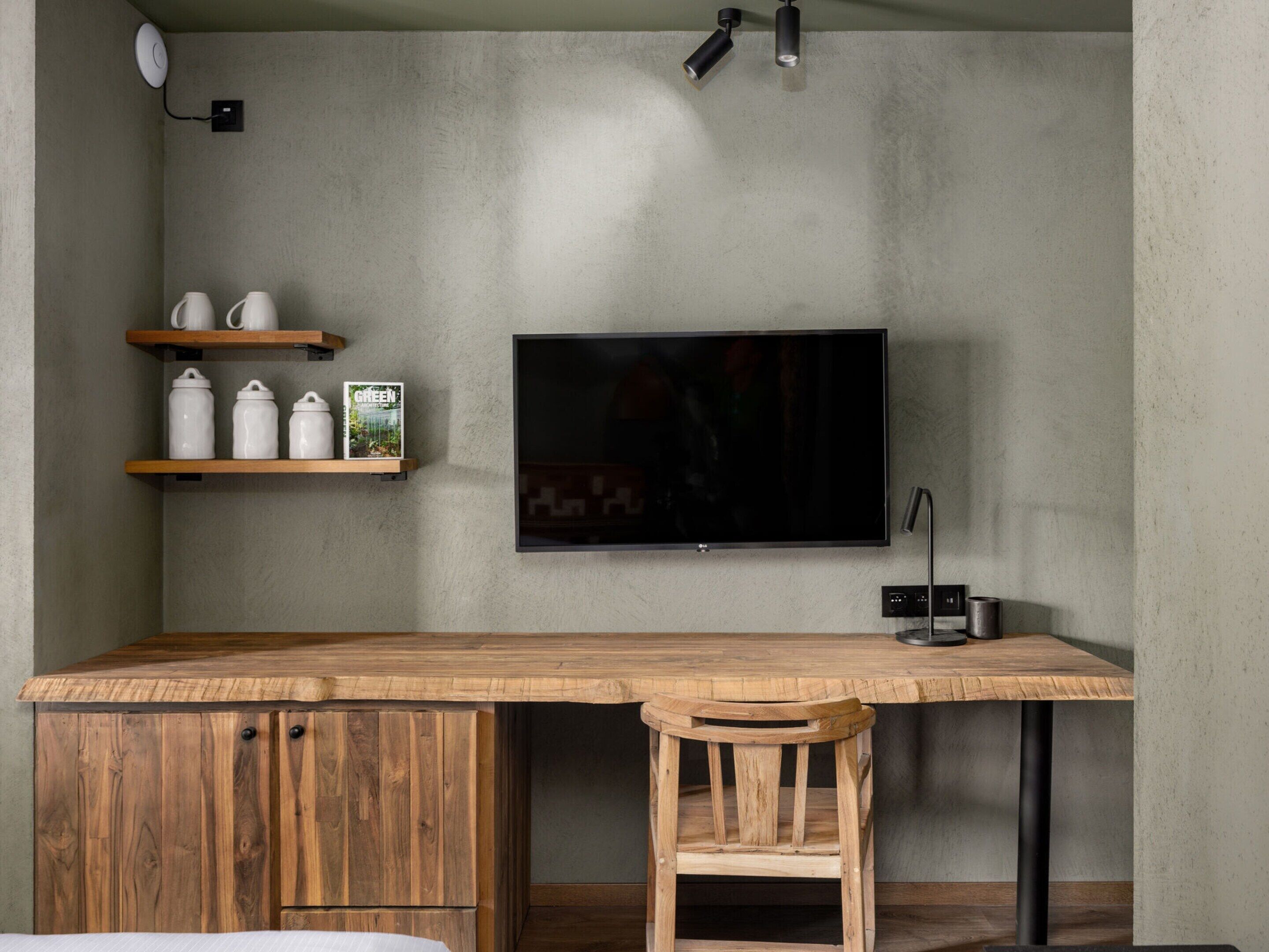 A modern kitchen with a wooden table, a TV mounted on the wall, and a shelf with kitchenware.