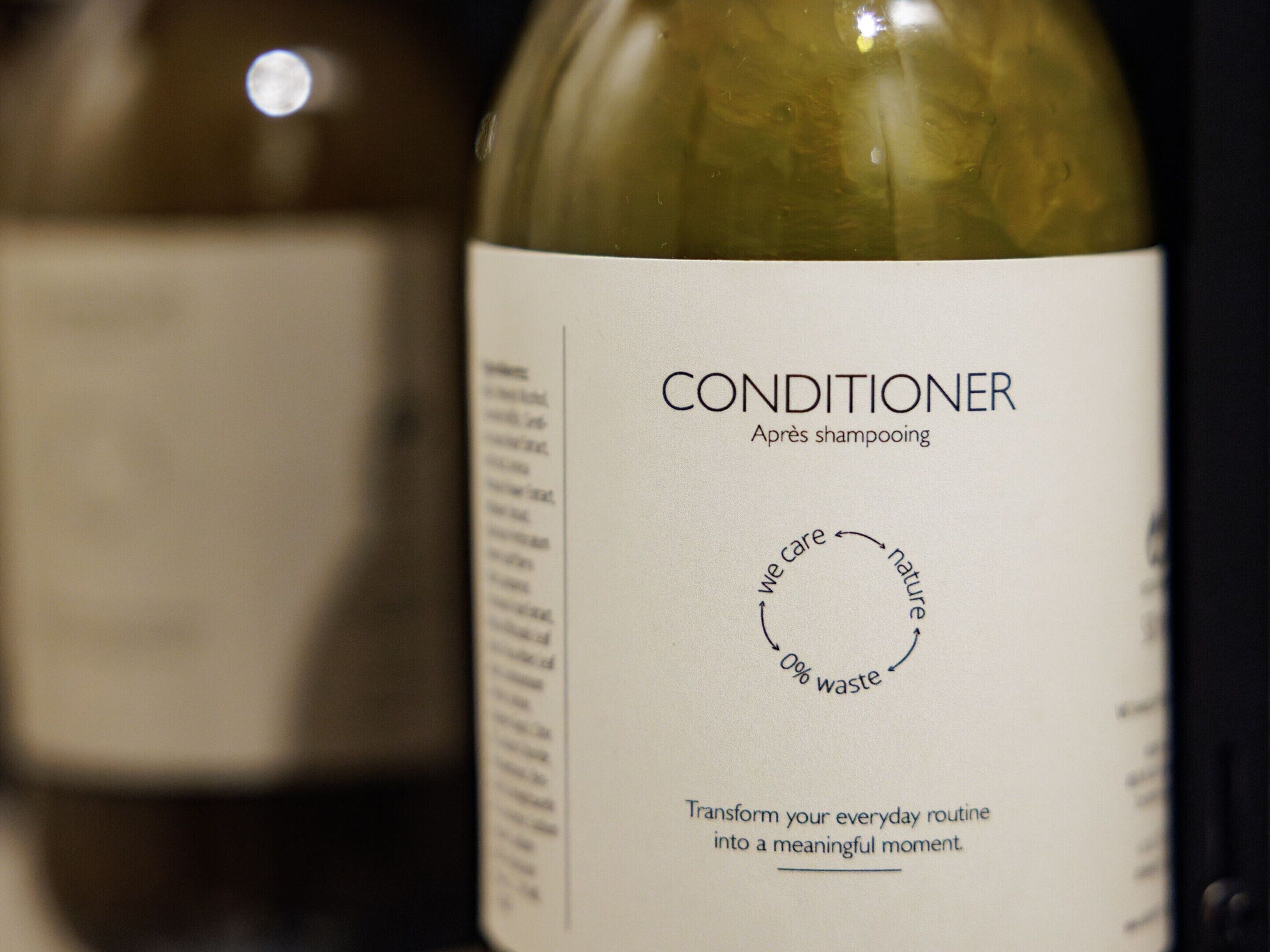 Een fles conditioner met een etiket waarop een cirkeldiagram en tekst staan over natuurbescherming en afvalvrij leven.