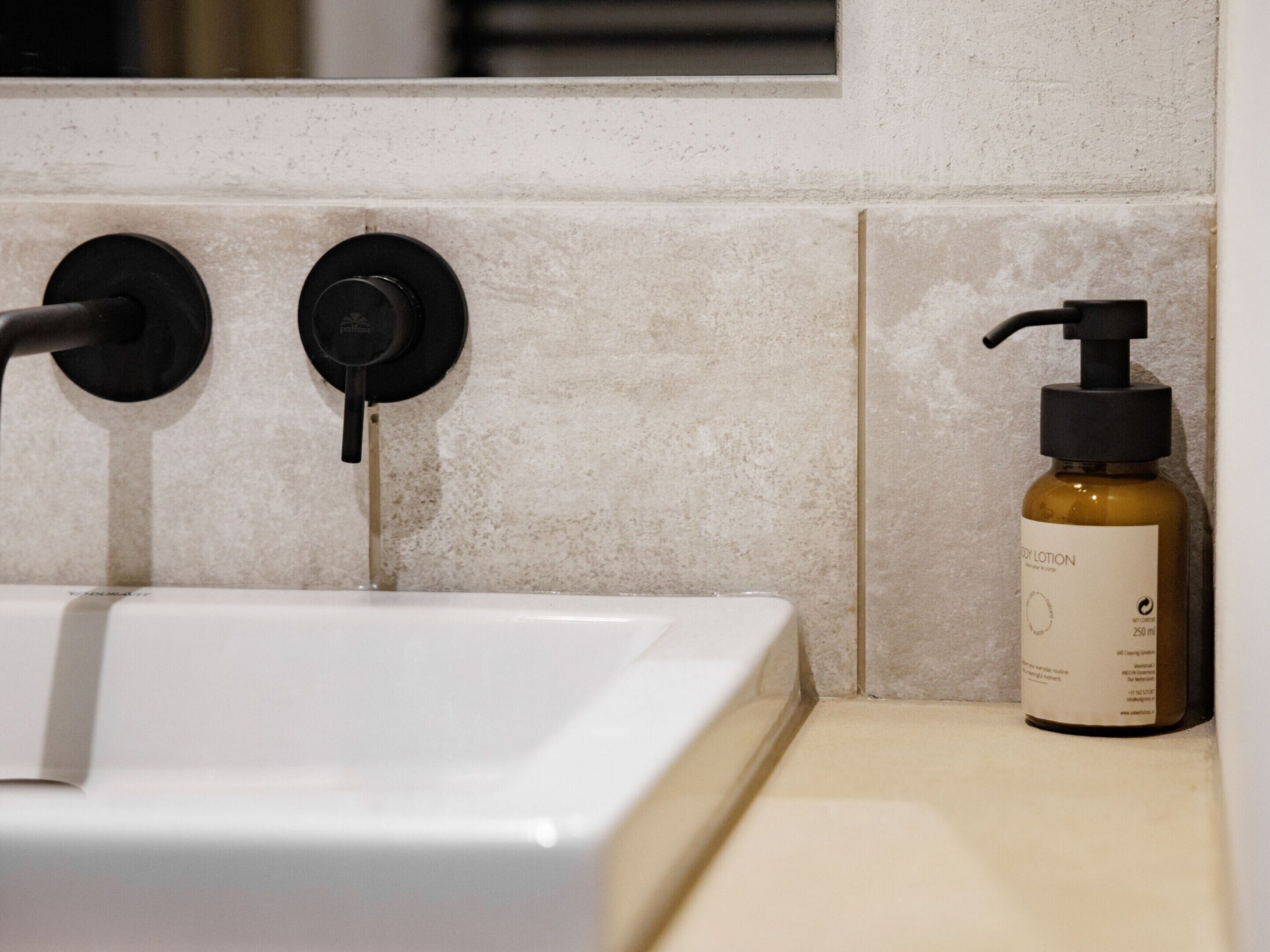 A bathroom with a white sink, black faucet, and a bottle of body lotion on the counter.
