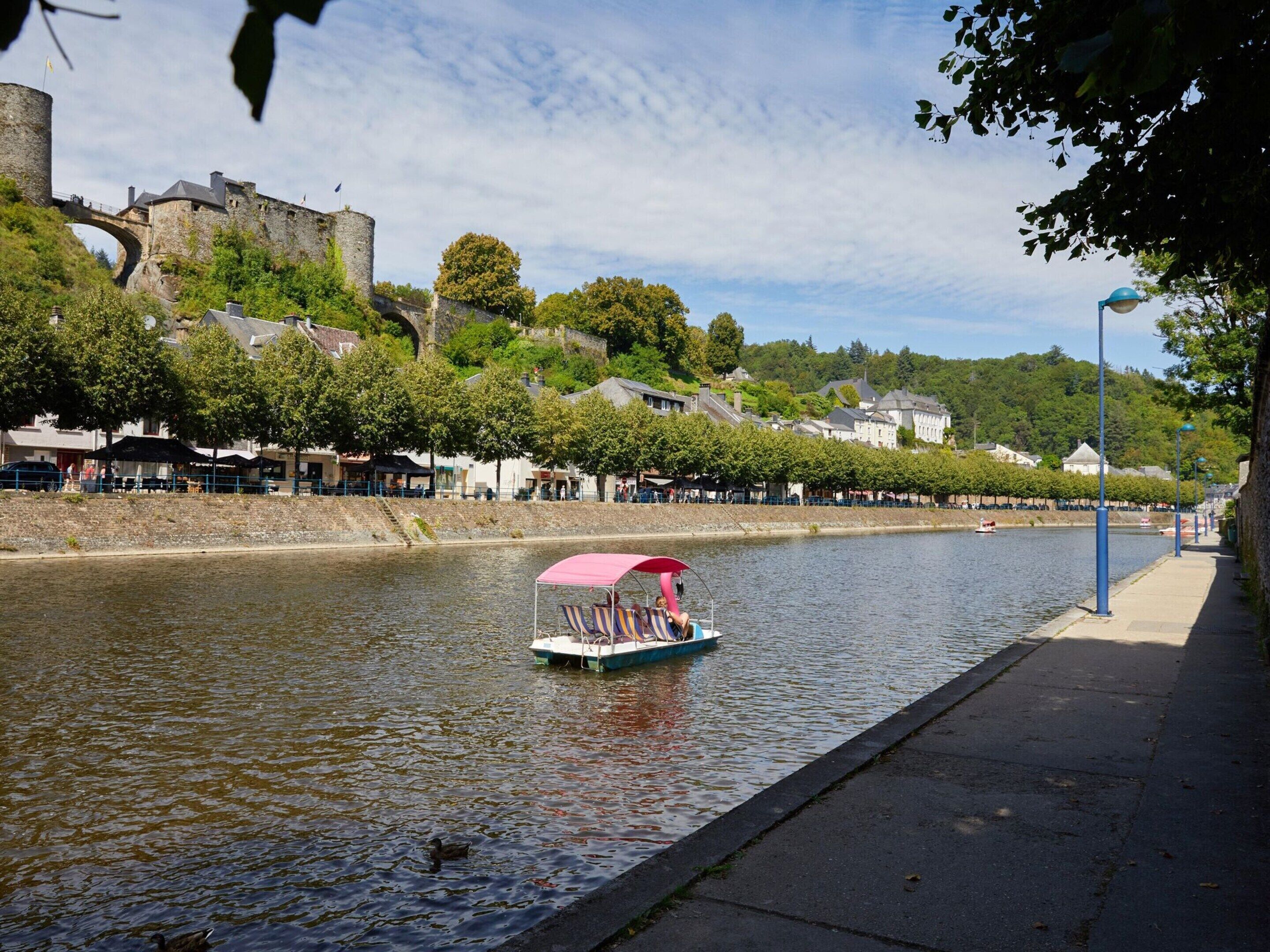 A river with a boat, a castle, and a tree-lined promenade.