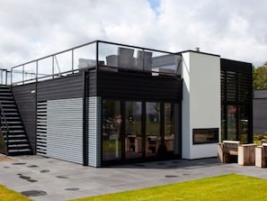 Un edificio moderno con cerramiento de vidrio, una escalera y mobiliario exterior.