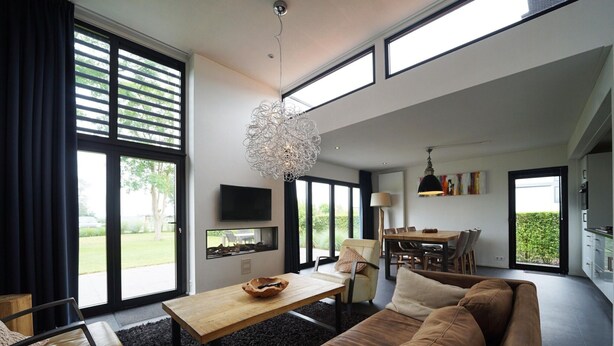 A modern living room with a large window, a dining area, and a kitchen. - Villa With Roof Terrace Near Veluwemeer (Nijkerk)