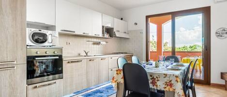 Una cocina moderna con electrodomésticos integrados, un comedor con una mesa dispuesta para dos personas y vistas al exterior a través de un ventanal.