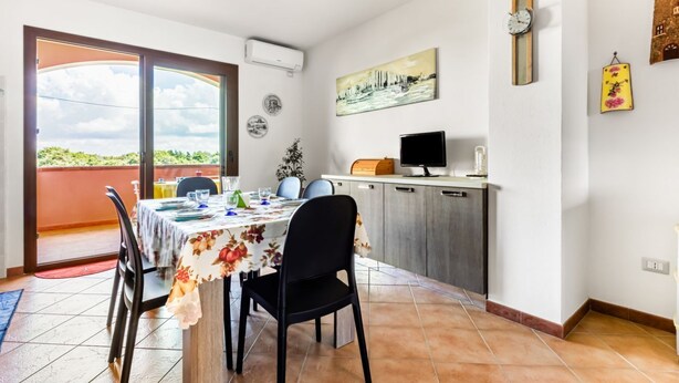A dining area with a table set for four, a kitchen with a TV, and a balcony with a view. - GuestHost - Sweet Home in Portoscuso! (Portoscuso)