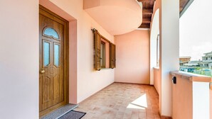 A corridor with a wooden door, a window with shutters, and a balcony with a railing. - GuestHost - Sweet Home in Portoscuso! (Portoscuso)