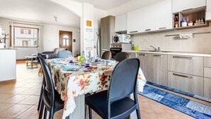 A modern kitchen with white cabinets, a microwave, and a sink. There is a dining table with chairs and a floral tablecloth. - GuestHost - Sweet Home in Portoscuso! (Portoscuso)