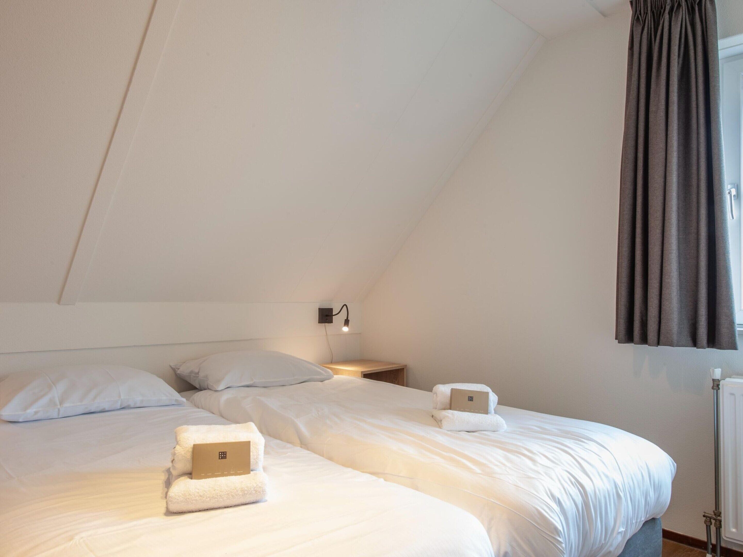 A bedroom with two beds, a nightstand, a wall-mounted lamp, and a radiator.