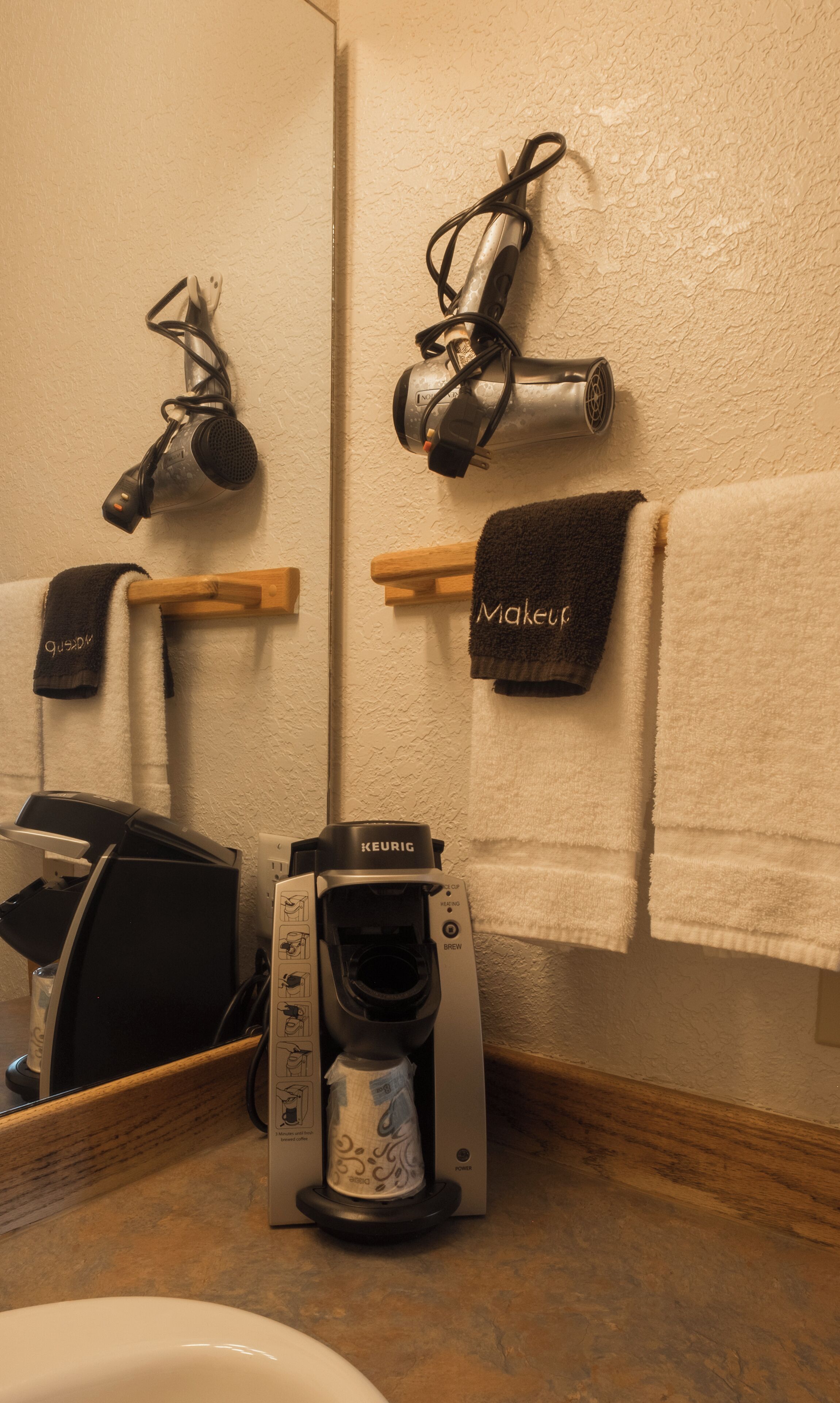 Une salle de bain équipée d’une machine à café, d’un sèche-cheveux et de serviettes suspendues sur un porte-serviettes.