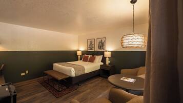 Una habitación de hotel con una cama, mesitas de noche con lámparas, una mesa redonda y una lámpara colgante.