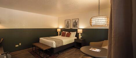 Una habitación de hotel con una cama, mesitas de noche con lámparas, una mesa redonda y una lámpara colgante.