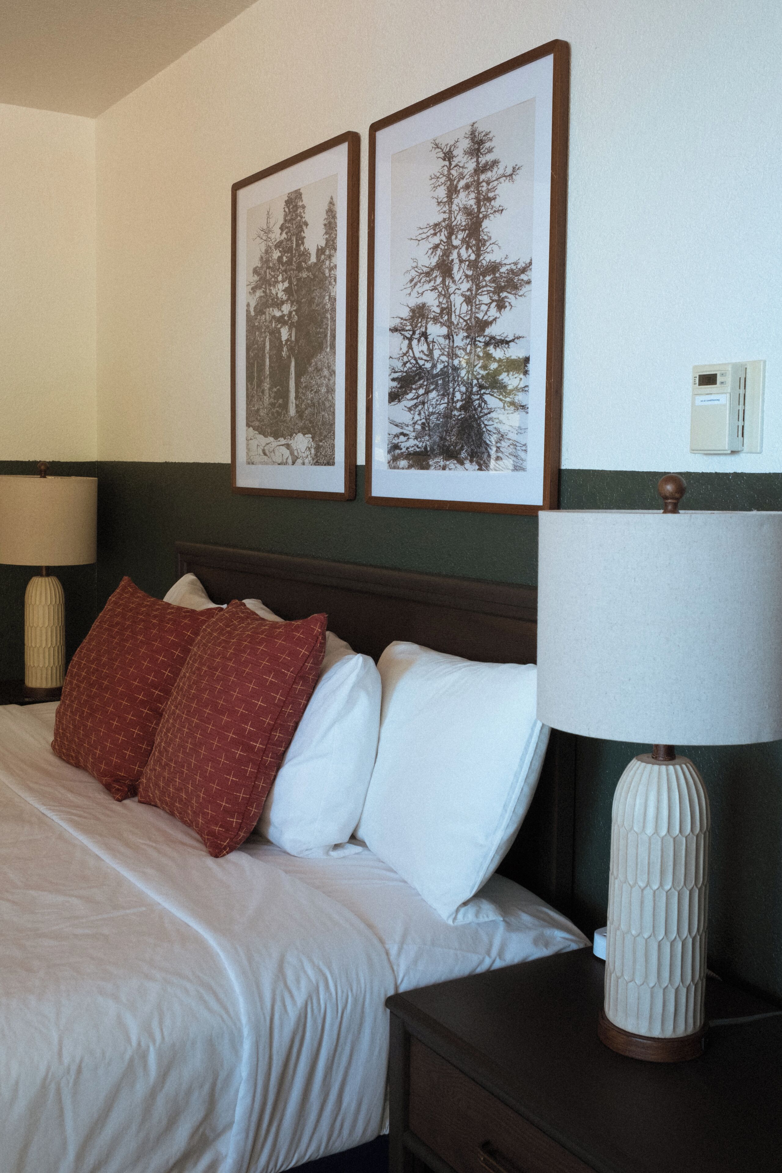 A neatly made bed with white and red pillows, a wooden headboard, and two framed pictures on the wall.