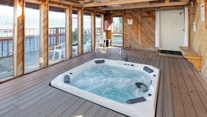 Een houten terras met een jacuzzi, houten wanden en grote ramen.