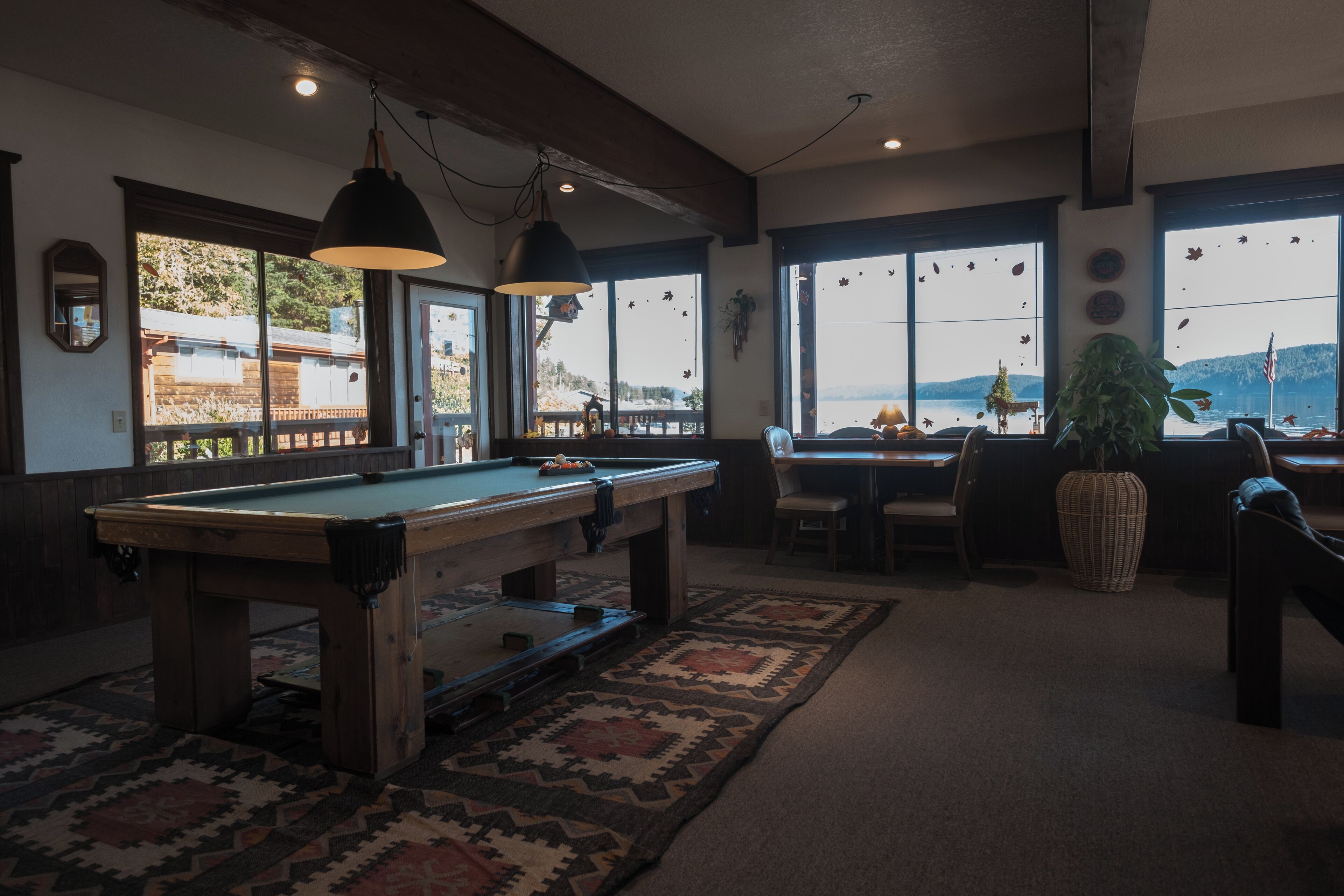 Una mesa de billar en una habitación con ventanas amplias, una zona de comedor y una planta.