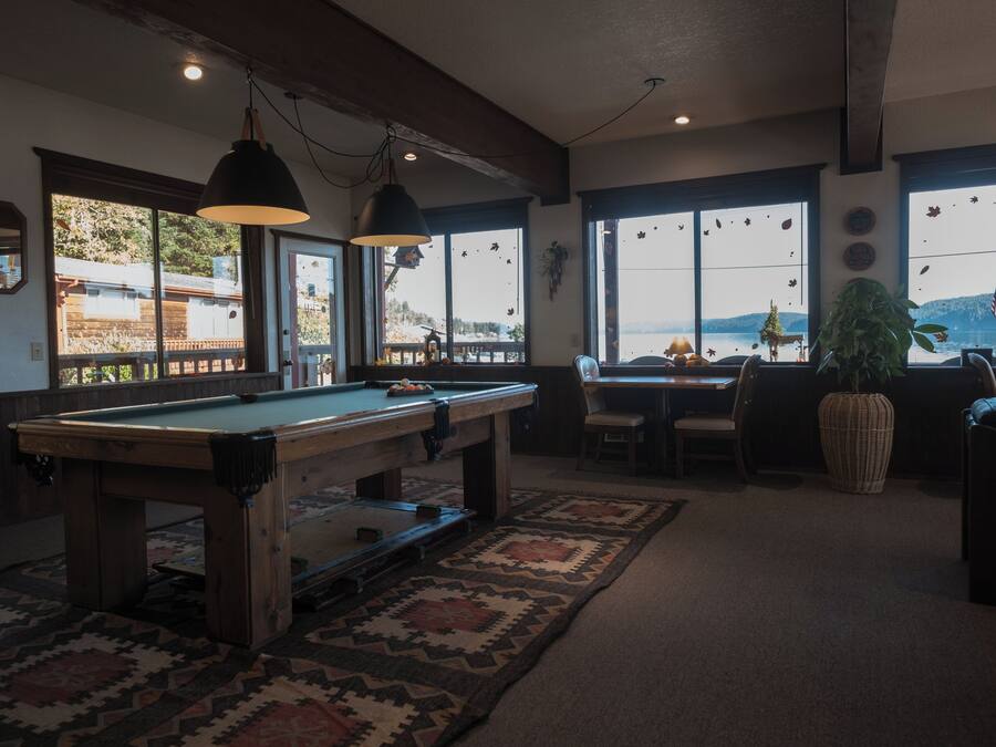 Una mesa de billar en una habitación con ventanas amplias, una zona de comedor y una planta.