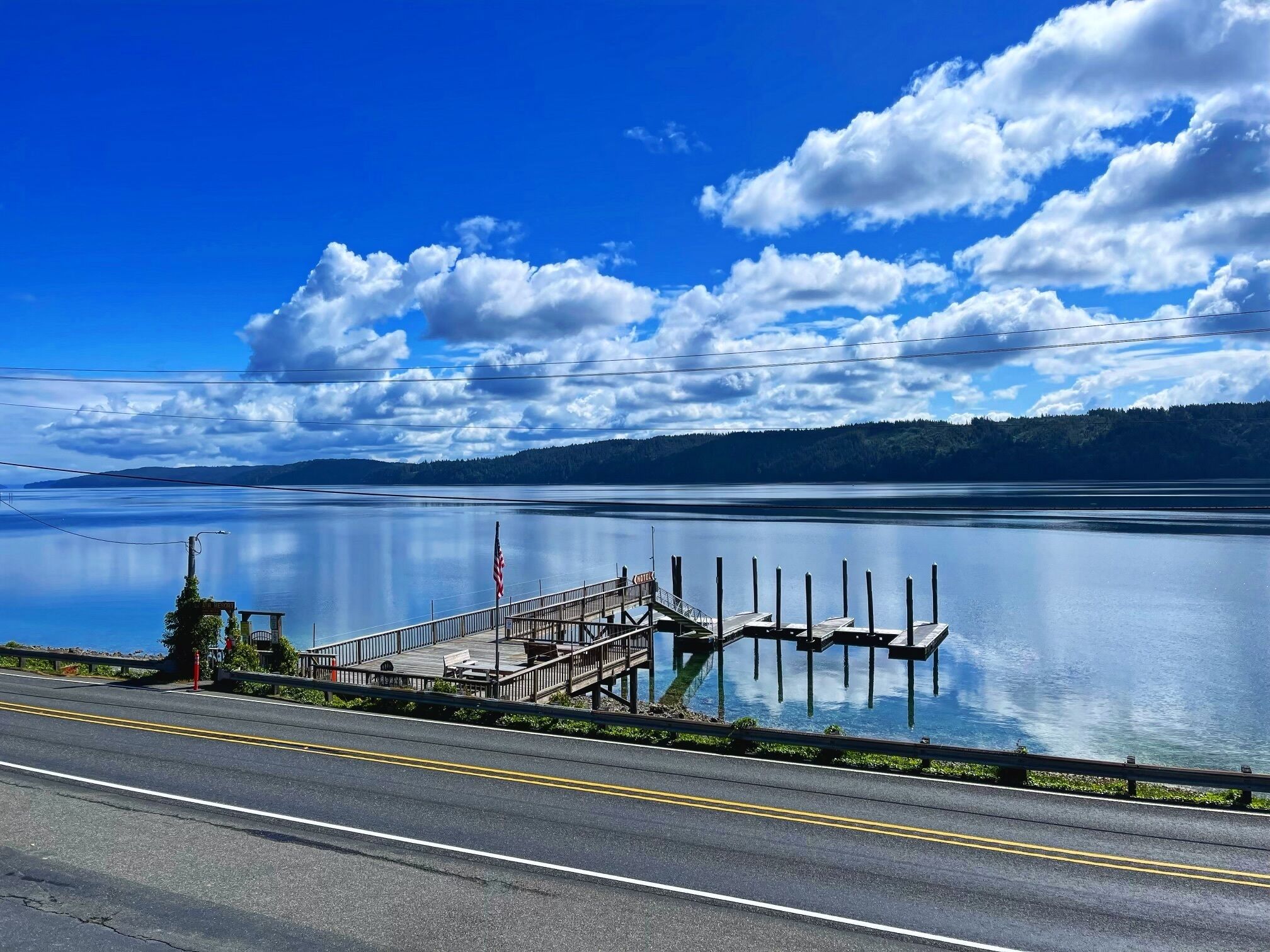 A calm lake with a dock extending into the water, surrounded by a forested landscape.