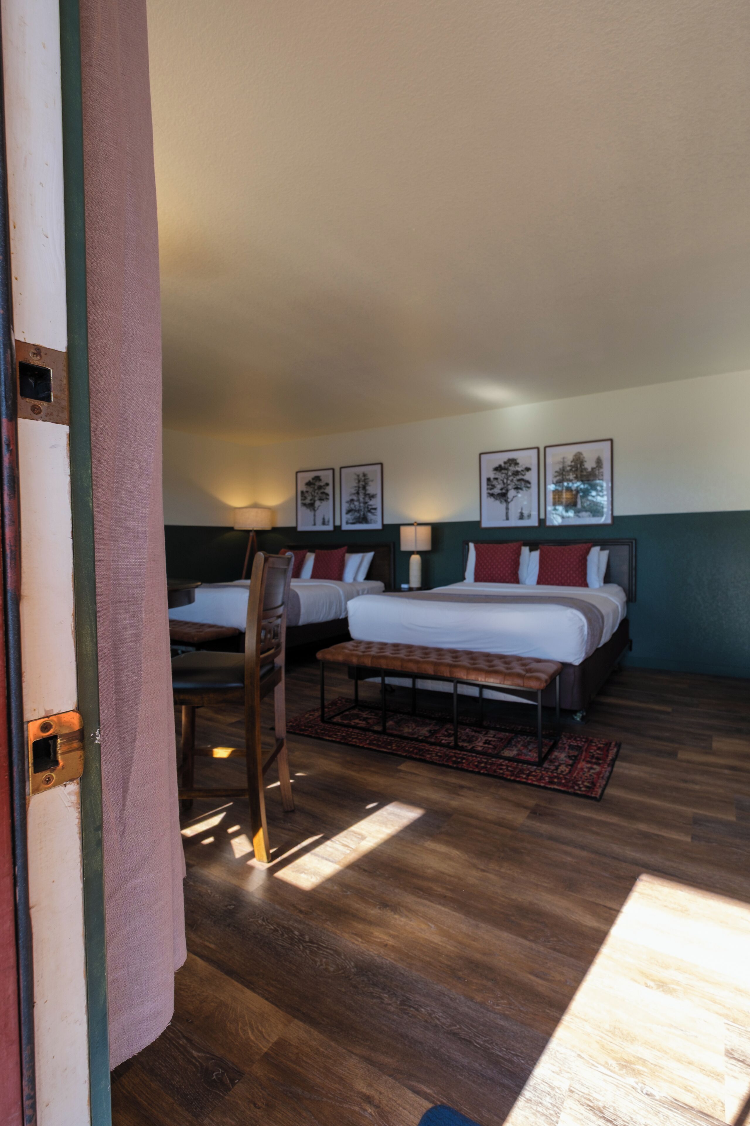A hotel room with two beds, a wooden floor, and a view of the outdoors.