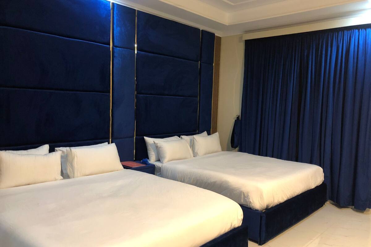 A hotel room with two beds, a large headboard, and a dark curtain.